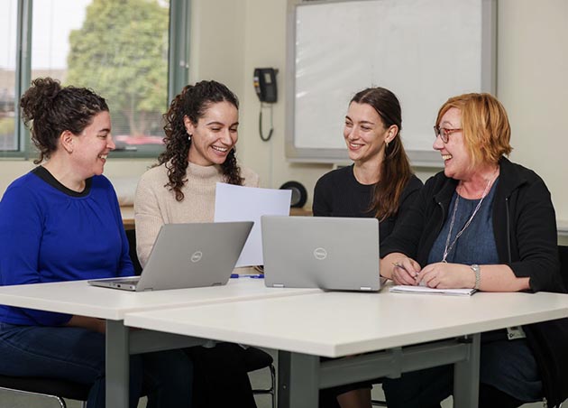 [GS17]: Four members of the IPC Health Autism Clinic sit at a table with laptops, smiling and discussing information on a piece of paper.