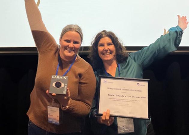 Two binGO MOVE staff face camera, raise an arm and are holding up the People's Choice Award and a Garmin card at the Australian Cardiovascular Health and Rehabilitation Association (ACCRA) Conference