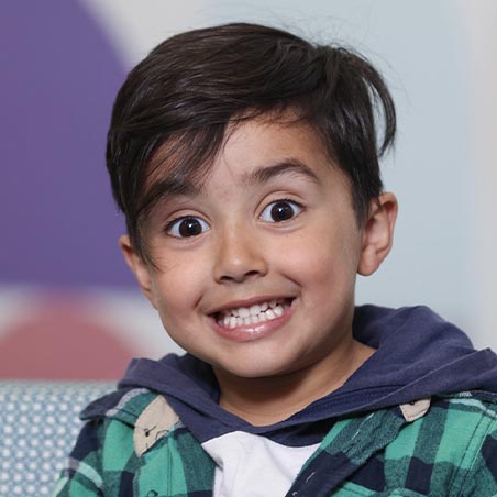 A young boy sits in a IPC Health reception with a very big smile.